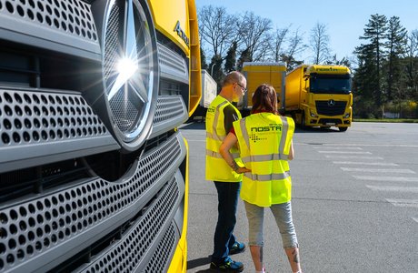 Zwei Personen in Warnweste auf einem Parkplatz vor dem LKW