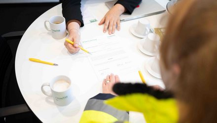 Zwei Personen sitzen gemeinsam an einem runden Tisch und bedienen gemeinsam ein Tablet auf dem NOSTA Jobs steht
