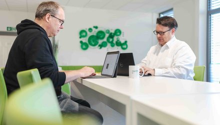 Zwei Kollegen sitzen sich gegenüber und arbeiten an ihrem Tablet.