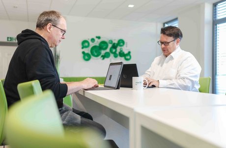 Zwei Kollegen sitzen sich gegenüber und arbeiten an ihrem Tablet.